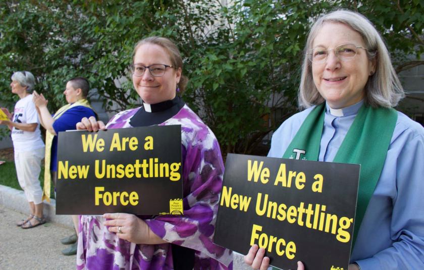 Two women hold signs saying We Are The New Unsettling Force
