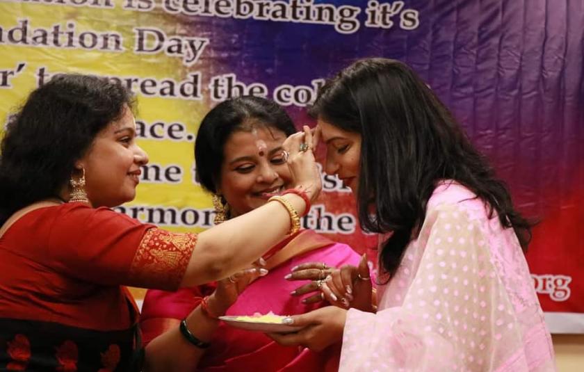 A woman puts tilak on another woman's forehead.