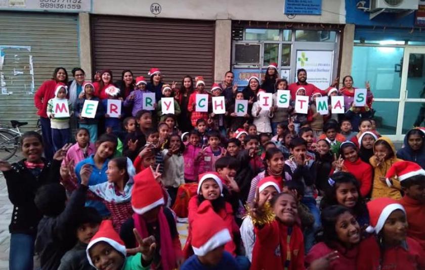 A group of children and adults in Christmas caps holding a banner which says MERRY CHRISTMAS.