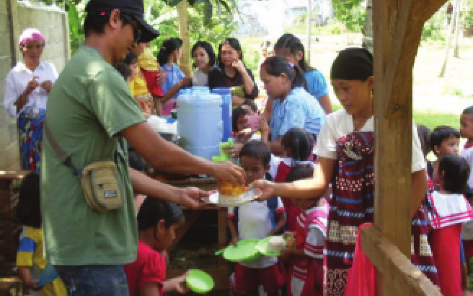 A young man is passing out food to children 