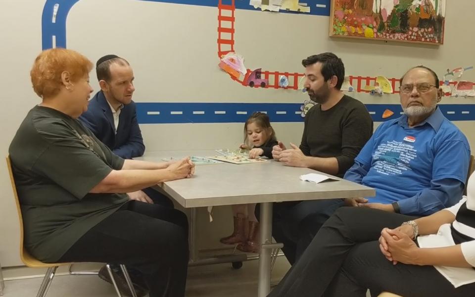 People sit in chairs around a table playing a board game. 