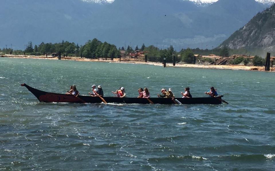 People sit in a canoe on a lake with mountains in the background.