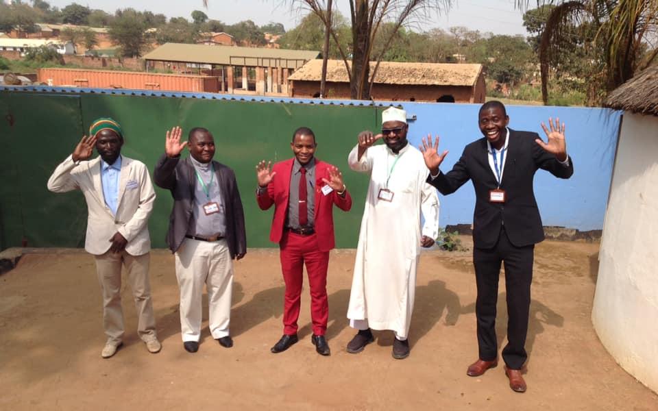 Photo: Five people standing in a row waving to the camera 