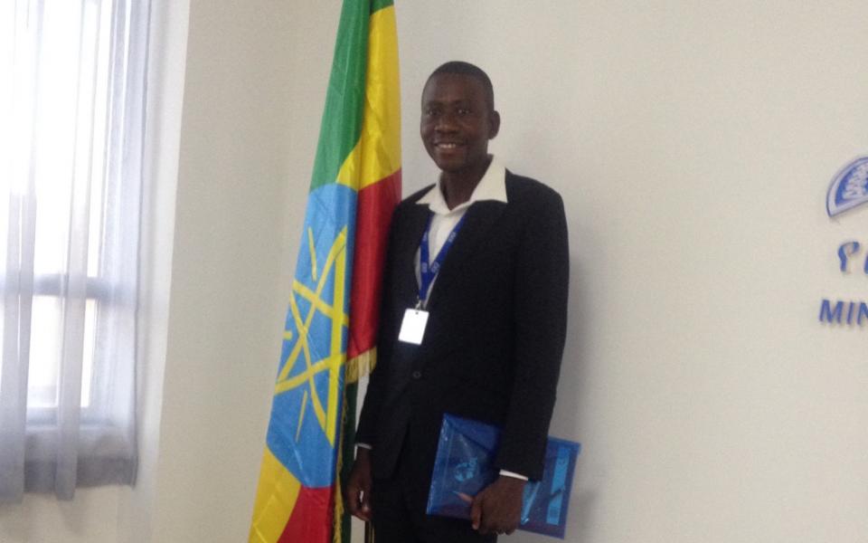 Photo: Geoffrey stands next to a flag, at the KAICIID Training in Addis Ababa