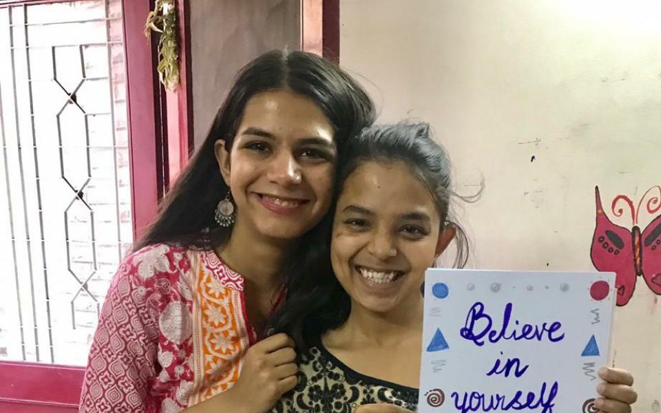 Two girls pose for a picture in which one girl is holding a piece of paper in her hand.